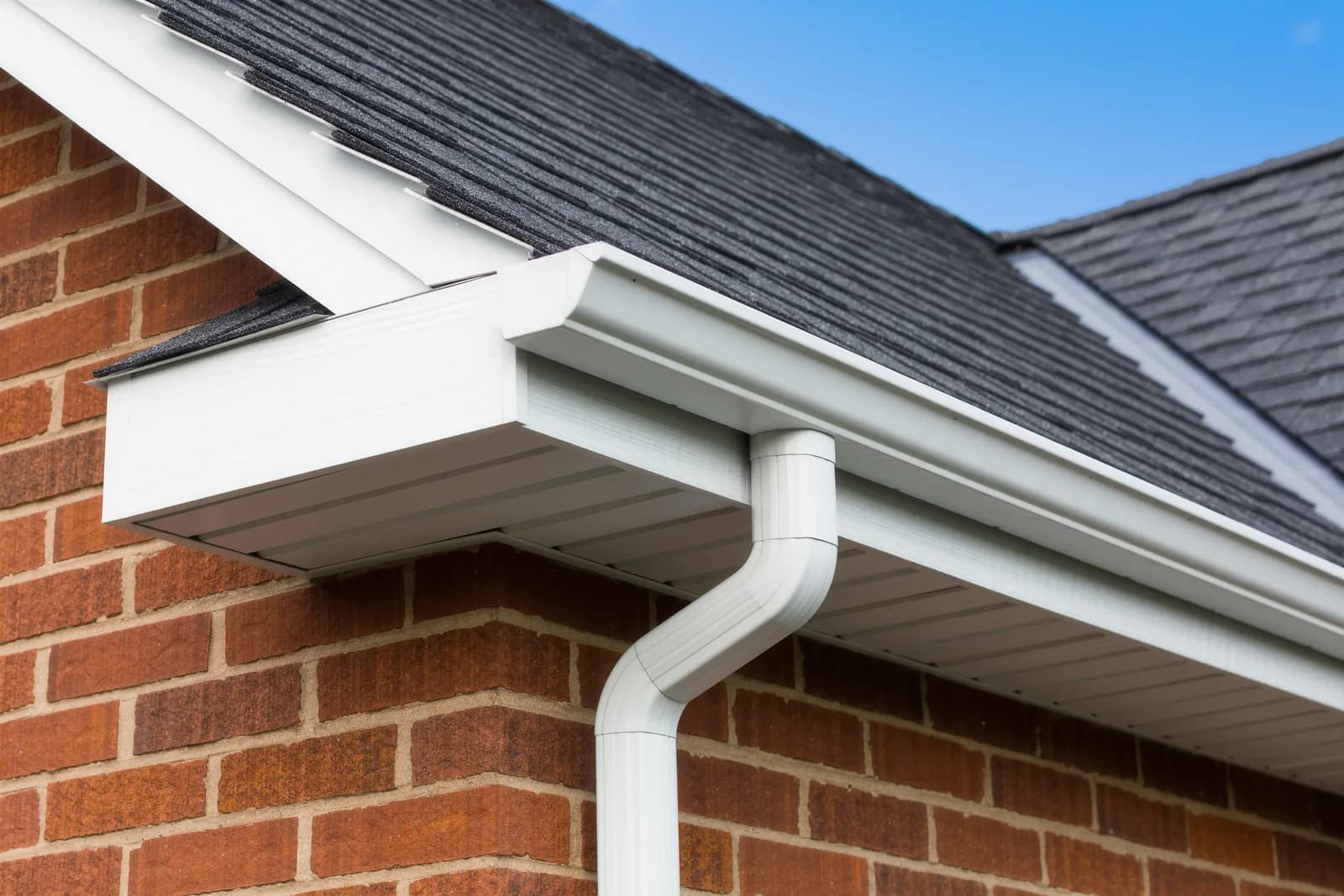 Newly installed white seamless aluminum gutters and downspout on a brick home with a new gray shingle roof